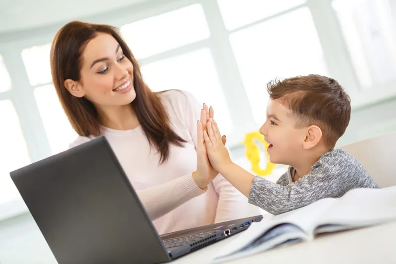 High-Five zwischen Nachhilfelehrerin und Kind am Laptop nach einem Lernerfolg
